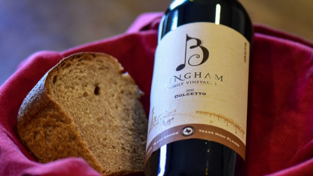 20.01.26_18Dolcetto_004-2-1200x675(16x9) | Bingham Family Vineyards Bottle of Bingham Family Vineyards Dolcetto next to a piece of homemade bread made with organic wheat grown at Bingham Farms