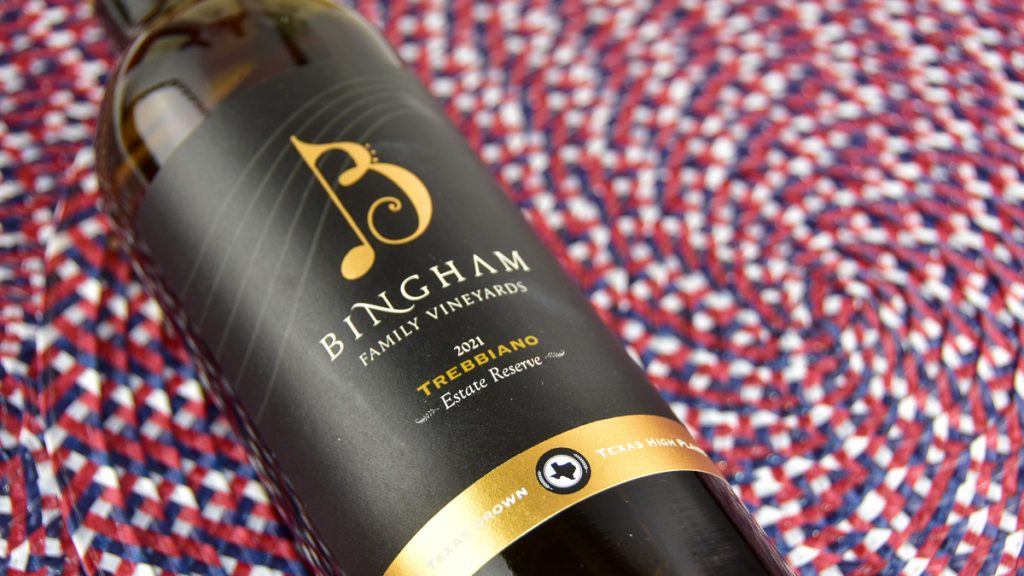 | Bingham Family Vineyards A bottle of Bingham Family Vineyards 2021 Reserve Trebbiano against a backdrop of red, white, and blue
