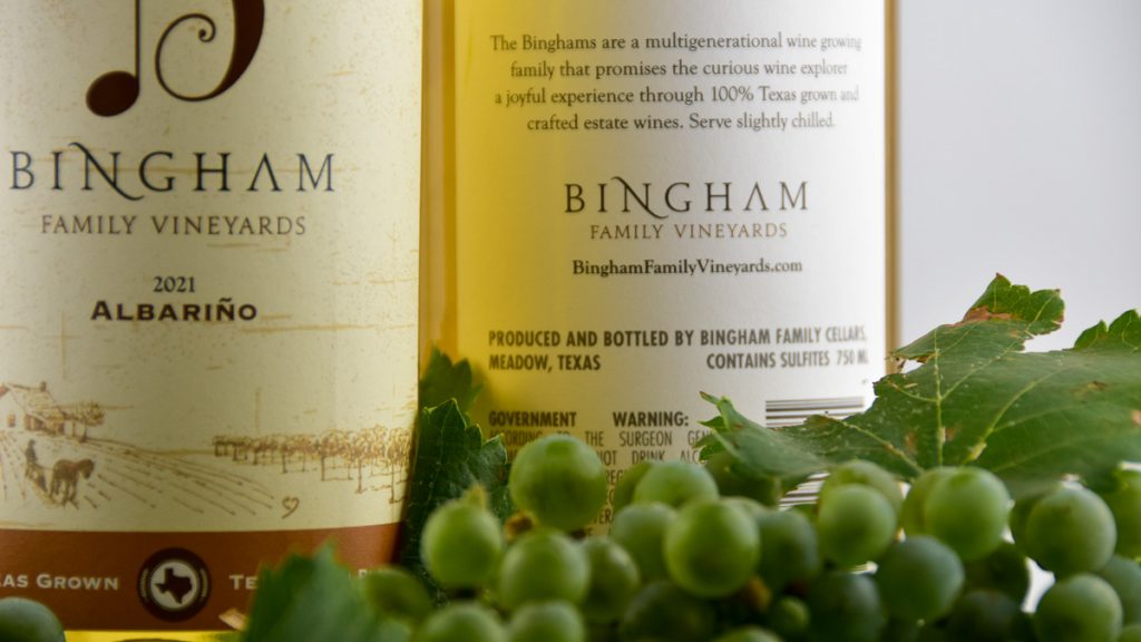 230801_Albarinobottletractor_002-1200-web-16x9 | Bingham Family Vineyards Albarino grapes grown at Bingham Family Vineyards in Meadow, Texas next to two bottles of Bingham Albarino wine