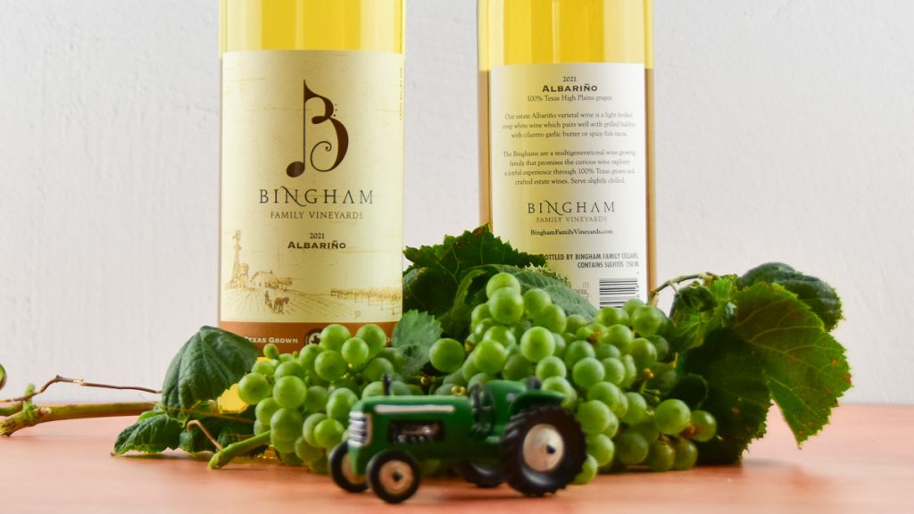 Albarino grapes grown at Bingham Family Vineyards in Meadow, Texas next to two bottles of Bingham Albarino wine and a toy tractor
