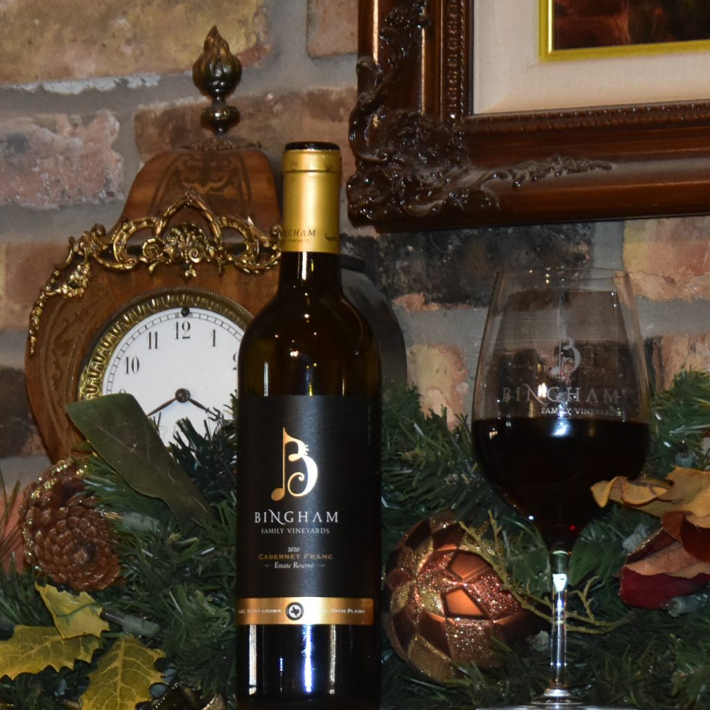 23.12.04_2020.R.Cab.Franc.Xmas_009.1200.web.1x1 | Bingham Family Vineyards bottle of Bingham Family Vineyards 2020 Reserve Cabernet Franc with glass of wine on a fireplace mantel with H