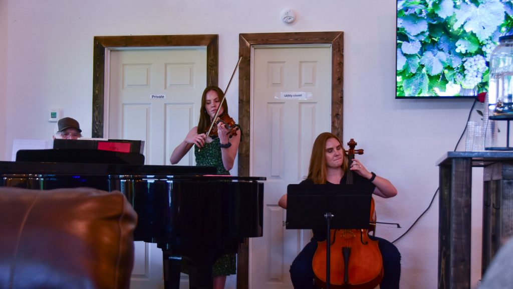 240408_HyeEclipse_052-1200-web-16x9 | Bingham Family Vineyards Cliff Bingham and two daughters playing music (piano, violin, cello) at Bingham Family Vineyards, Hye, Texas, tasting room