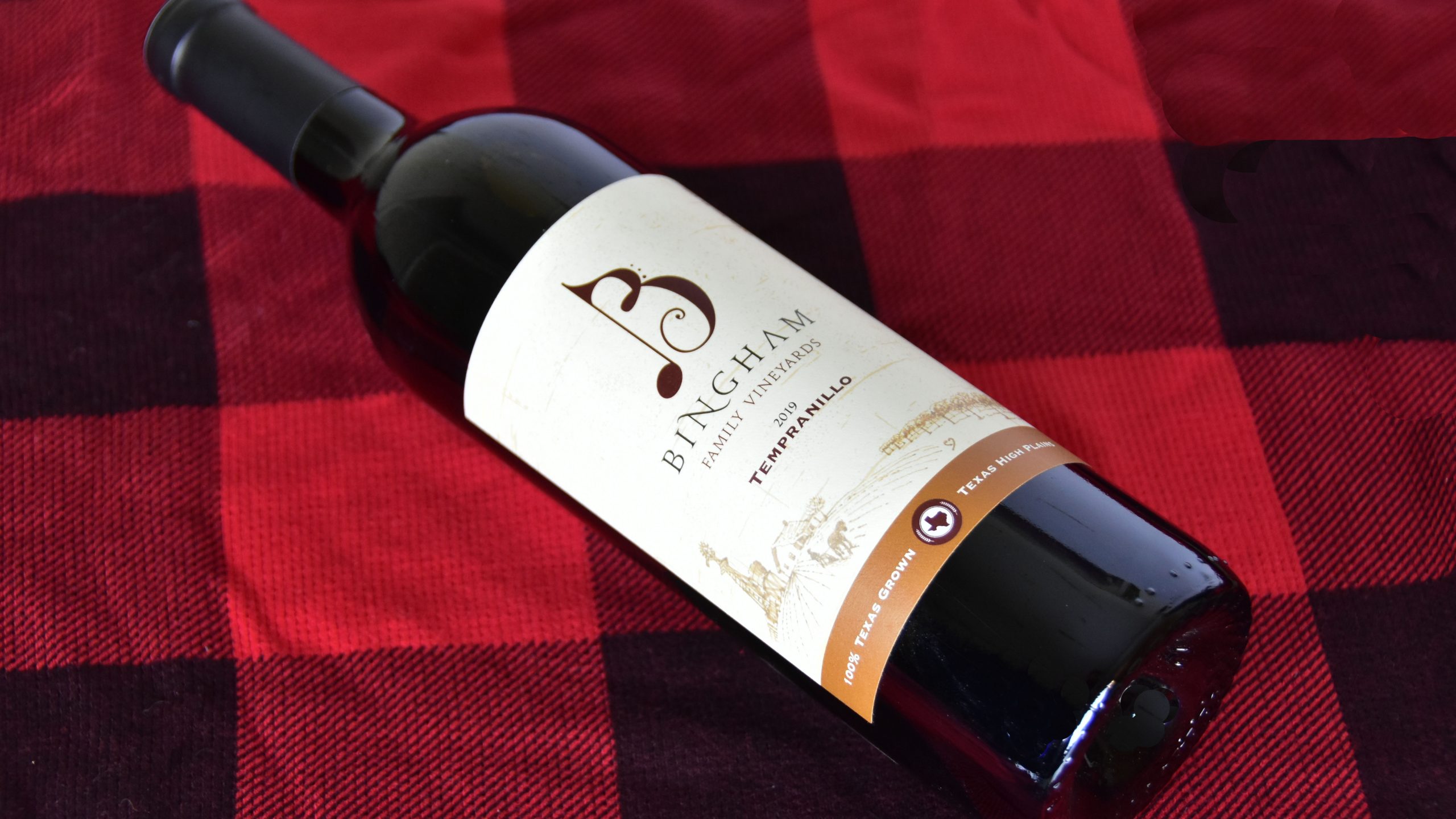 Bottle of Bingham Family Vineyards 2019 Tempranillo lying on red and black plaid material.