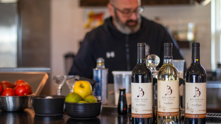 Chef Sage from Chef's House, Roanoke, Texas cooking with three bottles of Bingham Family Vineyards wine at the forefront of the photo.
