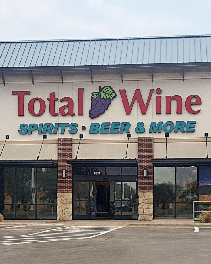 Total Wine and More Lubbock 4x5 | Bingham Family Vineyards Front of a Total Wine & More liquor store with a large red 'Total Wine' sign and grape logo, blue 'Spirits • Beer & More' lettering, brick facade, glass doors, and a parking lot in the foreground.
