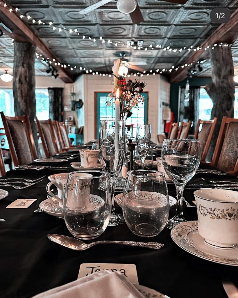 Long banquet table set for a formal dinner, with glassware, teacups, and a centerpiece under string lights in a rustic room.", Vintage Cork, Ben Wheeler, Texas