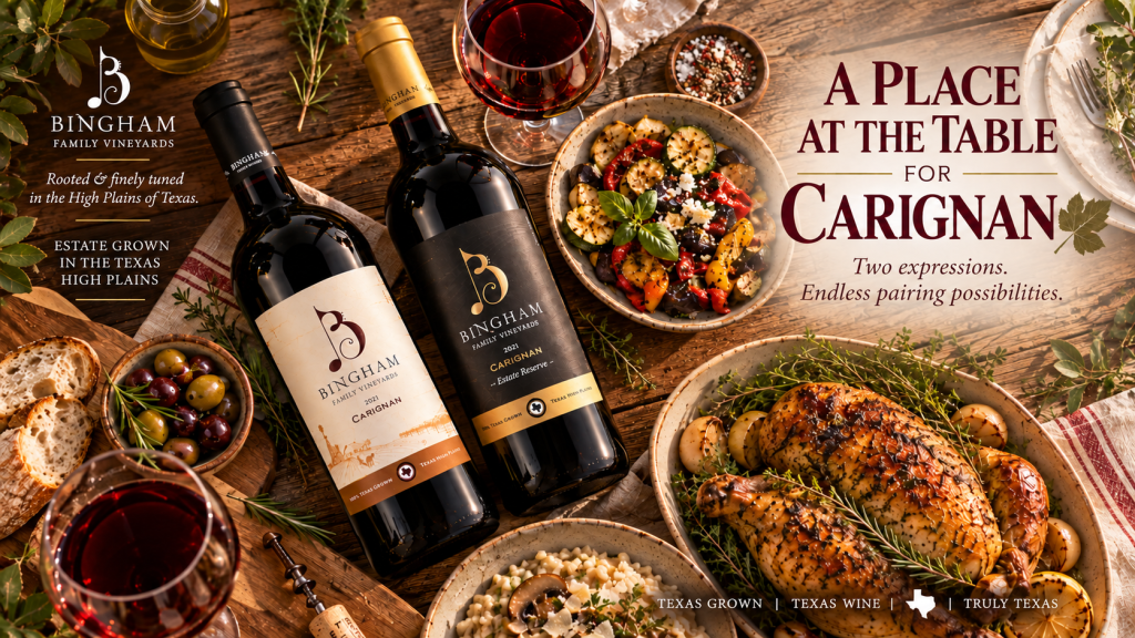 Overhead view of Bingham Family Vineyards 2021 Carignan and 2021 Estate Reserve Carignan bottles on a rustic dinner table with red wine, herb-roasted chicken, mushroom risotto, vegetables, and fresh herbs. Text reads “A Place at the Table for Carignan” and “Two expressions. Endless pairing possibilities.”
