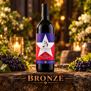 Bingham Family Vineyards 2021 Star Petit Verdot, Bronze award winner at the 2026 San Francisco International Wine Competition, displayed on rustic stone with dark grape clusters, greenery, white flowers, and warm candlelight.