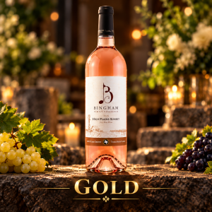 Bingham Family Vineyards 2025 High Plains Sunset Rosé, Gold winner at the 2026 San Francisco International Wine Competition, displayed on rustic stone with grape clusters, greenery, and warm decorative lighting.